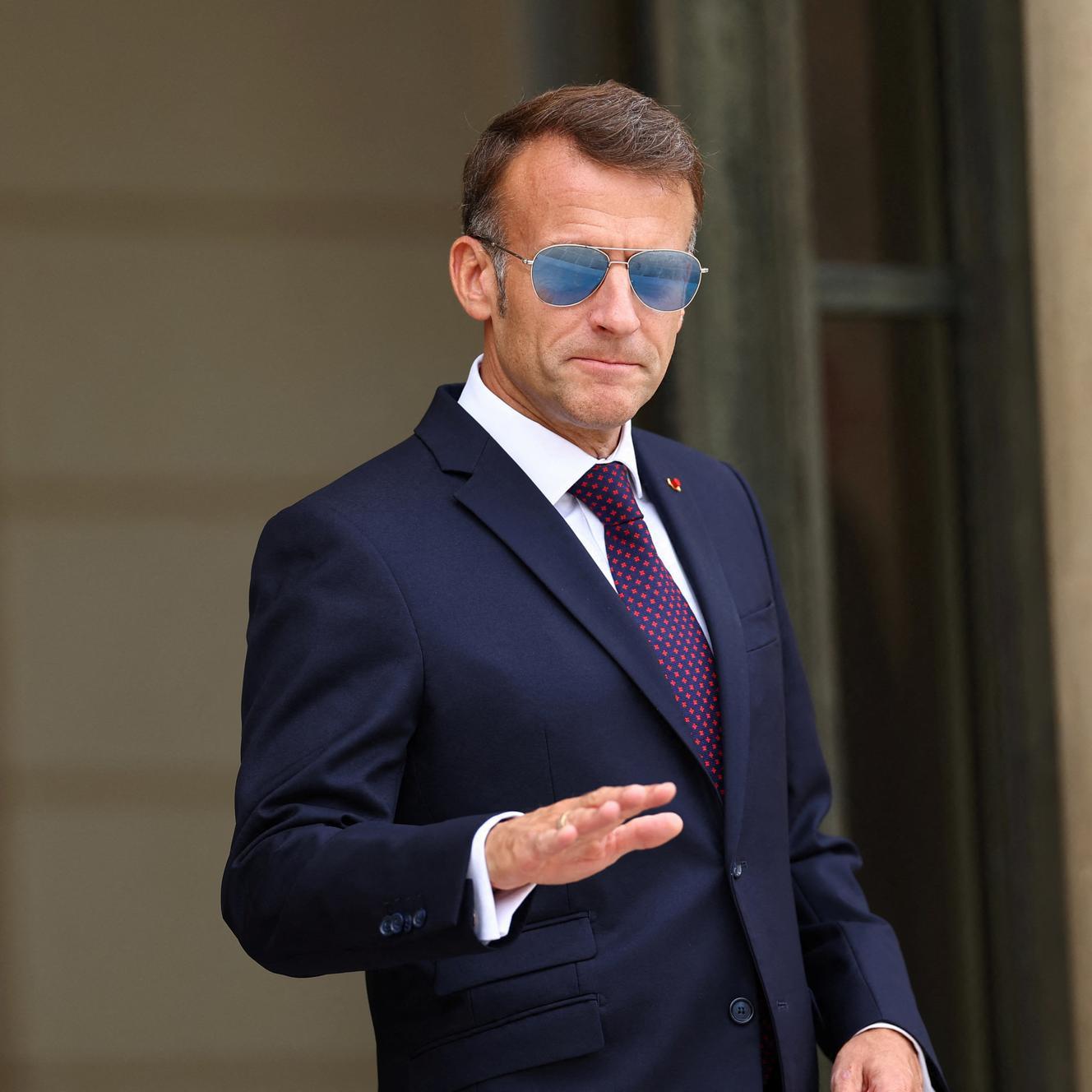 Photo de macron en costume et lunettes rayban.
Il tend la main comme si il disait mollo